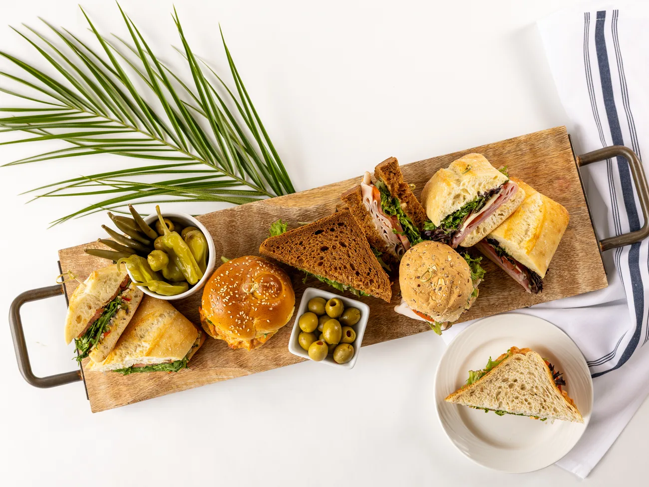 Wooden board of ciabatta, rye, and brioche sandwiches with olives and pickled peppers, prepared by Park Hospitality