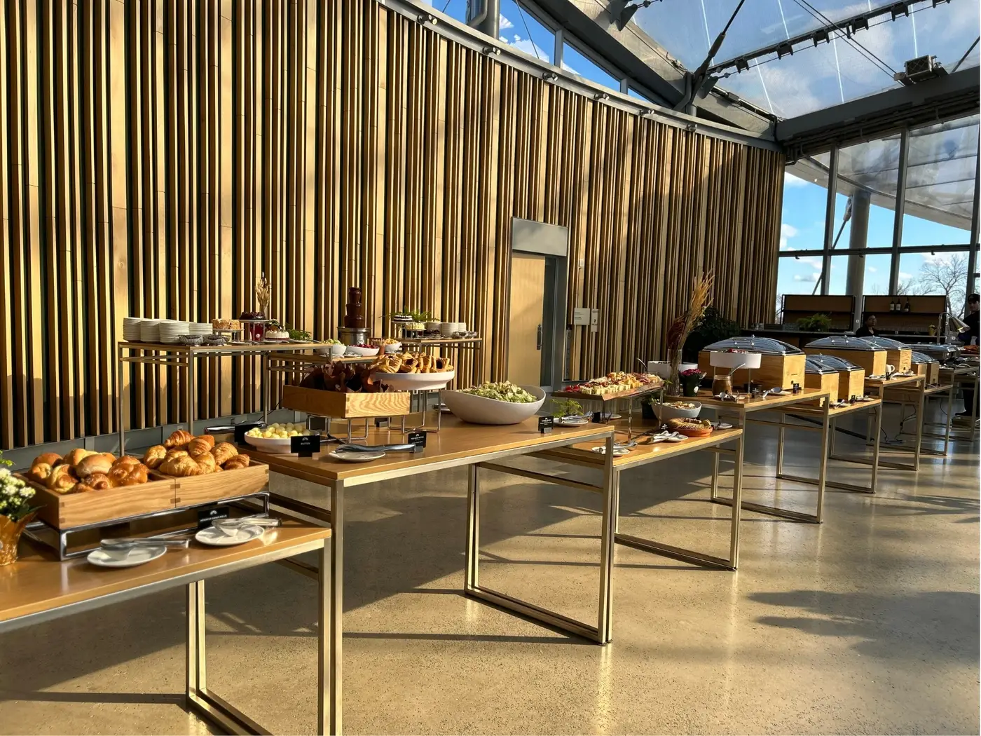 Buffet tables of pastries, canapés, salads, and chafing dishes set up beneath The Leaf's glass roof at Assiniboine Park