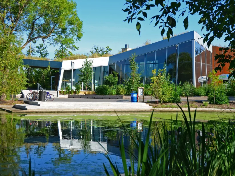 The Qualico Family Centre reflected in the Riley Family Duck Pond behind park trees at Assiniboine Park
