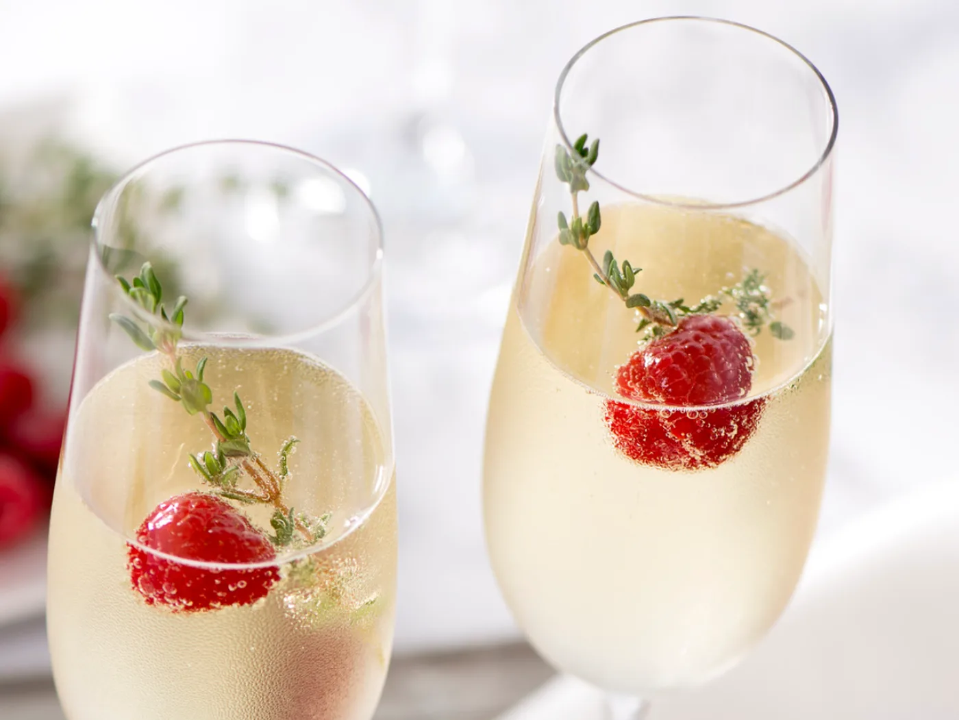 Two flutes of sparkling wine garnished with raspberries and thyme, poured for a toast