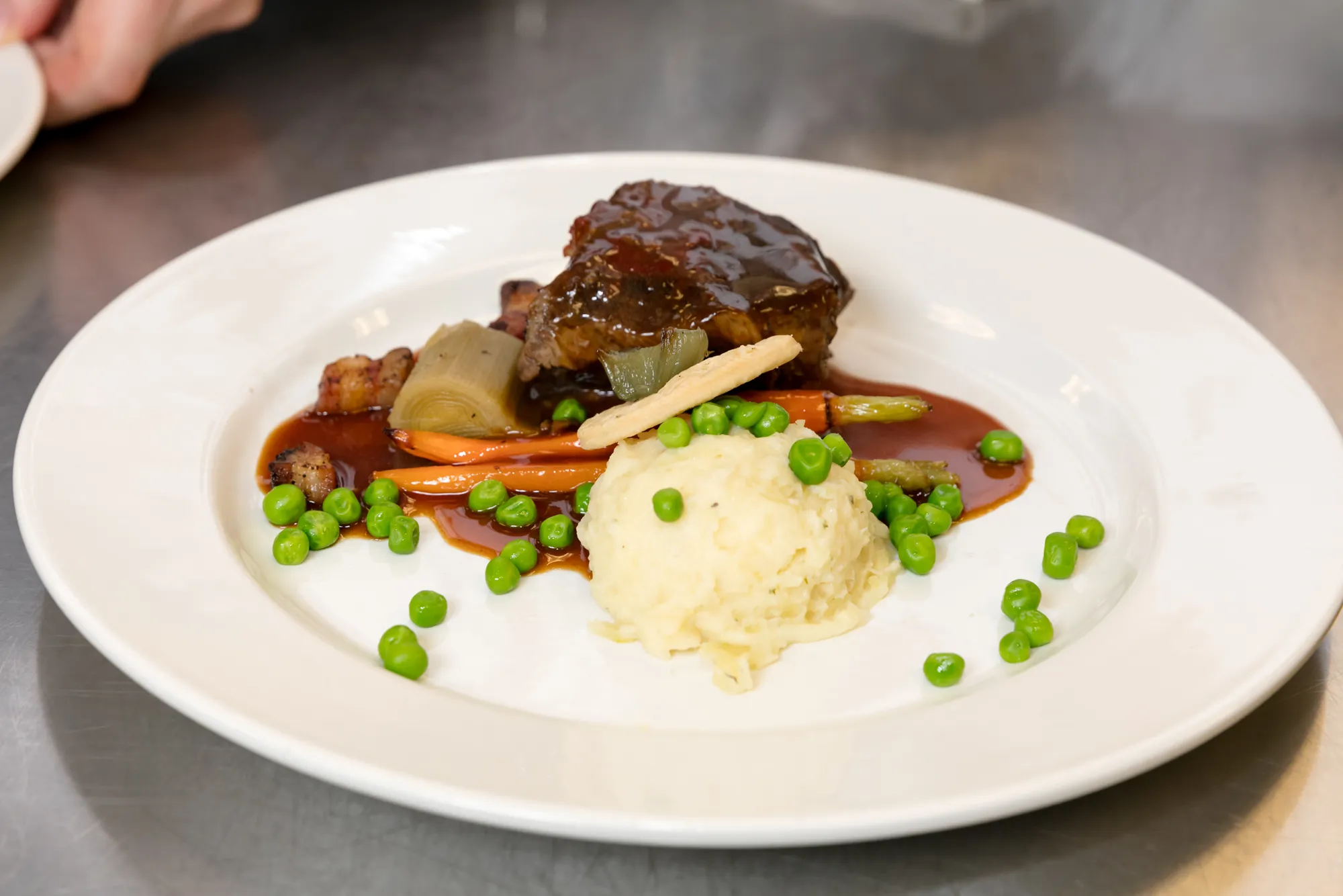Plated braised short rib dinner with mashed potatoes, carrots, and peas, prepared by Park Hospitality for a wedding reception
